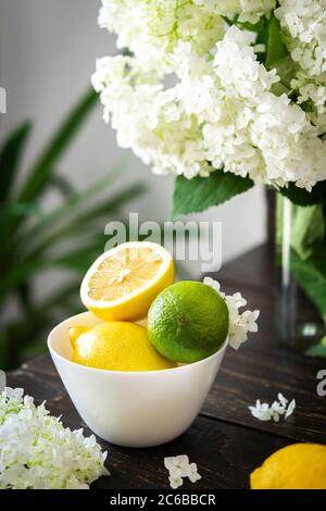 Vase de fleurs viburnum opulus Roseum et assiette avec citrons et lime Banque D'Images