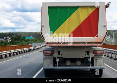 Gros camion avec le drapeau national de la République du Congo se déplaçant sur la route, sur le fond du village et du paysage forestier. Concept Banque D'Images