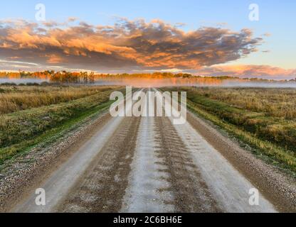 Une route de terre au lever du soleil, Ouest du Manitoba, Canada. Banque D'Images