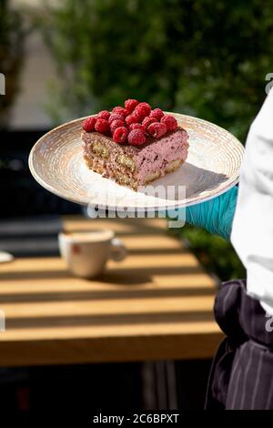 Tiramisu avec framboise dans les mains d'un serveur, matin, aube. Banque D'Images
