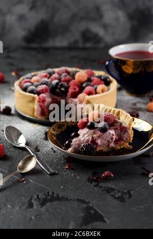 Gâteau au fromage maison aux framboises, aux mûres et aux raisins de Corinthe avec thé au karkade sur fond noir Banque D'Images