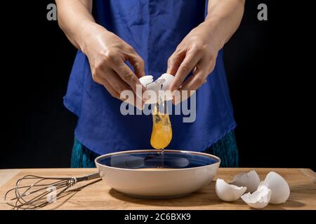 Une femme se fend et l'oeuf et le jaune tombe au bol. Banque D'Images