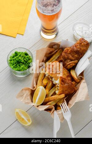 Frites et poisson frit. Repas avec des petits pois, de la salade, des citrons et de la bière Banque D'Images