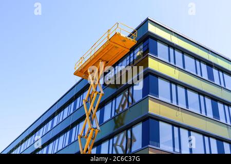 réparation moderne de la façade de bâtiment à l'aide d'un élévateur à ciseaux haut avec une plate-forme Banque D'Images