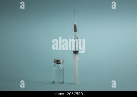 Petite bouteille de vaccin (flacon) et une seringue médicale injectable isolée sur fond bleu pour la vaccination en vue de la prévention, de l'immunisation et du traitement du vir Banque D'Images