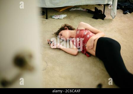 Une jeune fille se pose sur le sol recouvert de moquette de sa chambre regarde son téléphone Banque D'Images