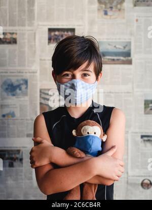 Jeune garçon portant un masque tenant un singe jouet avec toile de fond de journal. Banque D'Images