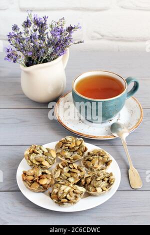 Biscuits de graines de citrouille enrobés de sucre sur une soucoupe et une tasse de thé aux herbes sur une table en bois gris. Gros plan Banque D'Images