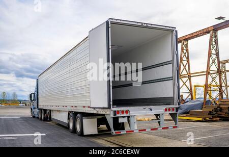 Camion semi-remorque bleu de qualité professionnelle avec porte ouverte semi-remorque vide se tenant sur le parking de l'entrepôt dans la zone industrielle en attente de la communication Banque D'Images