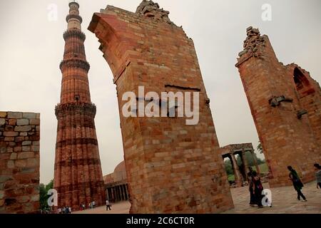 Les touristes qui marchent à travers la porte restante de la mosquée Quwat-ul-Islam avec Qutab Minar dominant en arrière-plan. Mehrauli, Delhi, Inde. Banque D'Images