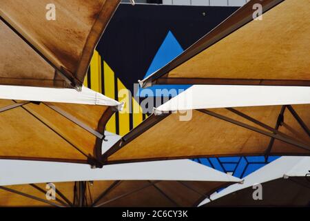 Parasols de marché rétroéclairés se chevauchant sur un marché artisanal de Melbourne avec un bâtiment bleu et jaune vif en arrière-plan Banque D'Images