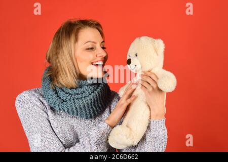 Une fille au visage souriant joue avec un jouet blanc doux. Tendresse et beauté concept. Une dame aux cheveux blonds regarde un adorable ours en peluche. La femme tient l'ours en peluche sur fond rouge. Banque D'Images