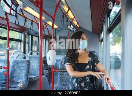 Jeune femme portant un masque de protection seul sur le bus, en regardant par la fenêtre. En s'appuyant sur l'une des barres. Concept de transport et de sécurité Banque D'Images
