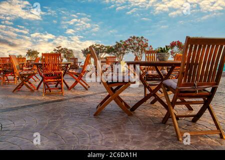 Terrasse extérieure d'un café avec chaises en bois vides et tables sur fond de ciel bleu coucher de soleil Banque D'Images