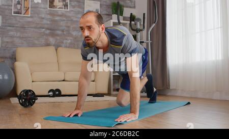 Faites travailler un homme qui fait du vélo tout terrain à la maison sur un tapis de yoga. Banque D'Images