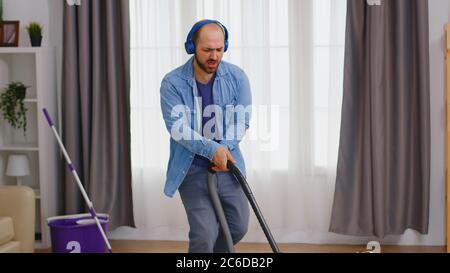 Homme écoutant de la musique sur un casque tout en nettoyant l'appartement avec aspirateur. Banque D'Images