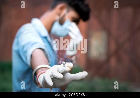 Homme tenant la cigarette sur sa main et se sentant coupable en situation de pandémie. Banque D'Images