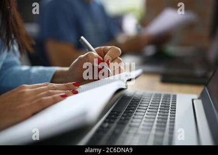 Une femme au bureau s'assoit au bureau et prend des notes dans un ordinateur portable. Affaires Banque D'Images