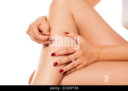 la jeune femme tire les poils sur ses jambes avec des pinces sur fond blanc Banque D'Images