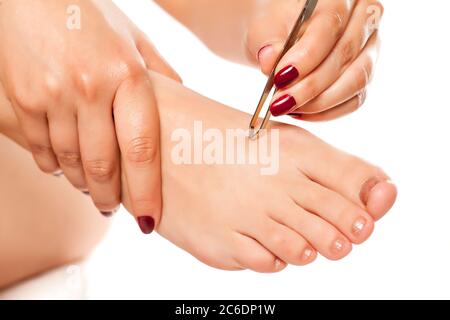 la jeune femme tire les poils sur ses pieds avec des pinces sur fond blanc Banque D'Images