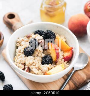 Bol de porridge d'avoine aux noisettes, de pêche et de blackberry servi avec une tasse de café. Un petit-déjeuner sain, la saine alimentation, régimes concept Banque D'Images