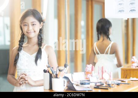 Portrait d'une jeune fille asiatique aux cheveux longs portant une robe de soirée blanche, souriant avec joie dans la salle de classe de maquillage Banque D'Images