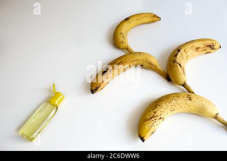 Concept créatif pour l'épidémie de coronavirus. Bouquet de bananes mûres à pois et bouteille ouverte de désinfectant jaune pour les mains. Table blanche avec espace vide Banque D'Images