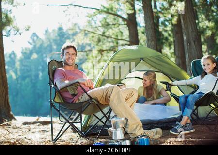 Famille souriante se détendre au camping dans les bois Banque D'Images