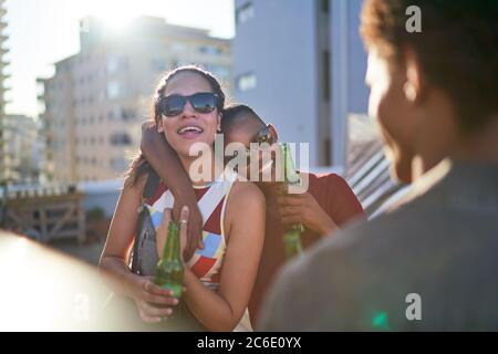 De jeunes amies joyeuses boivent de la bière sur le toit ensoleillé de l'été Banque D'Images