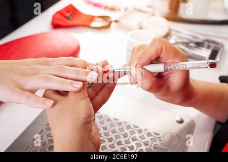 La femme lubrifie les ongles du client avec une brosse. Le processus de manucure dans un salon de beauté. Salon en noir, rouge, blanc. Le maître de manucure pu Banque D'Images