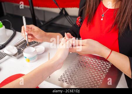 La femme lubrifie les ongles du client avec une brosse. Le processus de manucure dans un salon de beauté. Salon en noir, rouge, blanc. Le maître de manucure pu Banque D'Images