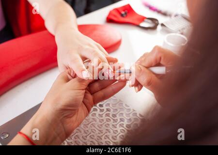 La femme lubrifie les ongles du client avec une brosse. Le processus de manucure dans un salon de beauté. Salon en noir, rouge, blanc. Le maître de manucure pu Banque D'Images