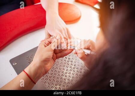 La femme lubrifie les ongles du client avec une brosse. Le processus de manucure dans un salon de beauté. Salon en noir, rouge, blanc. Le maître de manucure pu Banque D'Images