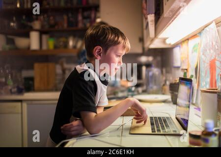 Garçon faisant ses devoirs à l'ordinateur portable sur le comptoir de la cuisine Banque D'Images