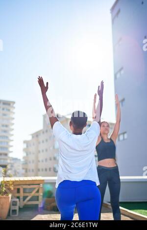 Jeunes femmes pratiquant le yoga sur le balcon urbain ensoleillé sur le toit Banque D'Images