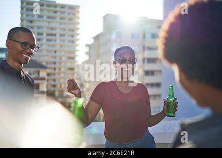 Des jeunes amis sans soucis dansent et boivent de la bière sur le toit ensoleillé Banque D'Images