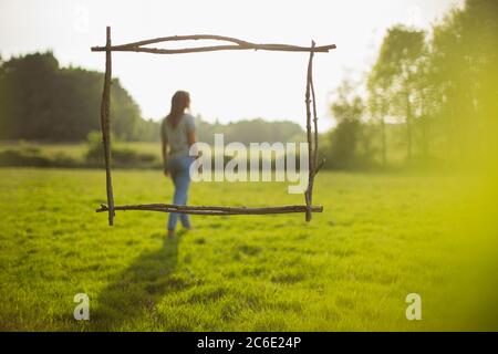 Cadre de branche sur une femme marchant dans un champ d'herbe ensoleillé idyllique Banque D'Images