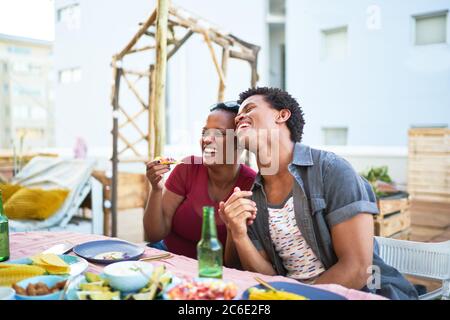 Un jeune couple heureux riant et mangeant à table de patio Banque D'Images