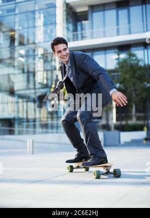 Homme d'affaires souriant skate à l'extérieur d'un bâtiment urbain Banque D'Images