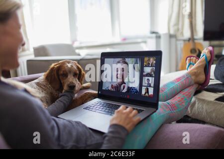 Femme avec un ordinateur portable, discutant vidéo avec des amis sur un canapé avec un chien Banque D'Images