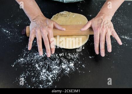 Femme roulant de la pâte avec la broche sur le comptoir de cuisine fariné Banque D'Images