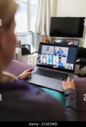 Femme avec un ordinateur portable, discutant vidéo avec des médecins depuis un canapé Banque D'Images