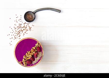 Smoothie Acai, granola, graines, baies fraîches dans un bol en bois. Assiette remplie de baies et cuillère en céramique sur fond de bois blanc. plat Banque D'Images