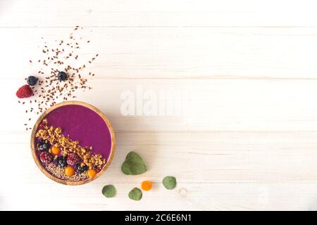 Smoothie Acai, granola, graines, baies fraîches dans un bol en bois. Assiette remplie de baies sur fond de bois blanc. Vue de dessus, dessus, plat Banque D'Images