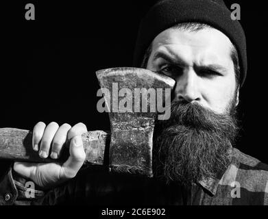 Bel homme ou bûcheron, hipster barbu avec barbe et moustache en hat détient old rusty lame de fer d'ax isolé sur fond noir Banque D'Images