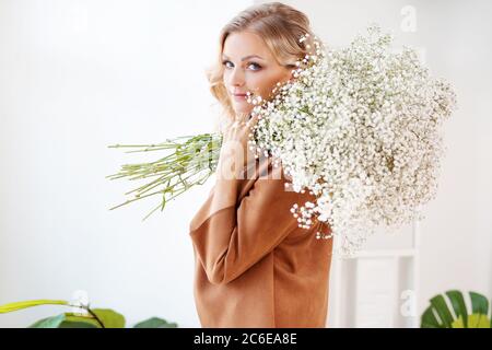 Jeune femme blonde élégante avec un bouquet de gitsophila. Portrait à l'intérieur. Happy Girl avec un bouquet de fleurs, livraison de fleurs. Banque D'Images