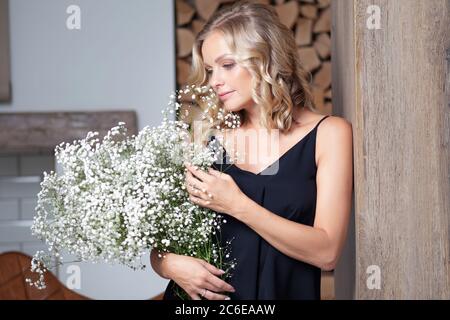 Jeune femme blonde élégante avec un bouquet de gitsophila. Portrait à l'intérieur. Happy Girl avec un bouquet de fleurs, livraison de fleurs. Banque D'Images