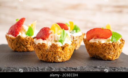 des gâteaux sains avec fromage cottage et fruits dans des paniers de flocons d'avoine sur un tableau noir et un fond blanc. des petits gâteaux Banque D'Images