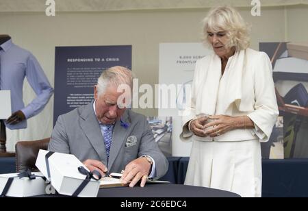 Le Prince de Galles, signant le livre des visiteurs, et la duchesse de Cornwall lors d'une visite à l'usine de chemises Turnbull et Asser à Gloucester pour rencontrer des membres du personnel. Au cours des premières étapes de la pandémie du coronavirus, la société a changé toute sa chaîne de production pour fabriquer des produits de nettoyage pour le NHS. Banque D'Images