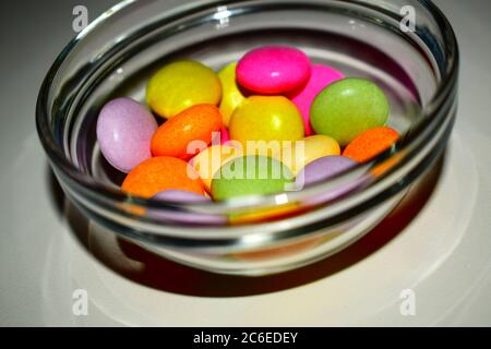 Groupe de petits bonbons de couleur mélangée dans un bol en verre transparent sur fond blanc Banque D'Images